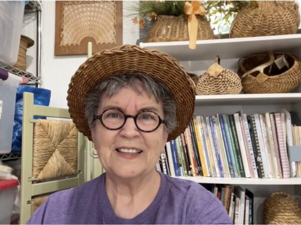 Cathryn Peters wearing a wicker hat in front of a bookcase