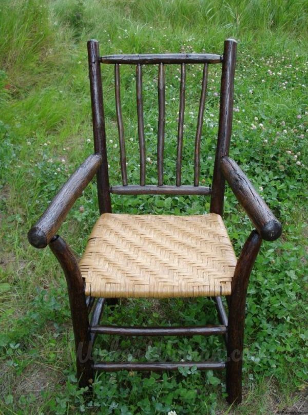 Dark colored rustic hickory arm chair with reed splint seat sitting on a grassy field.