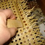 using a wooden caning wedge to press cane webbing into groove