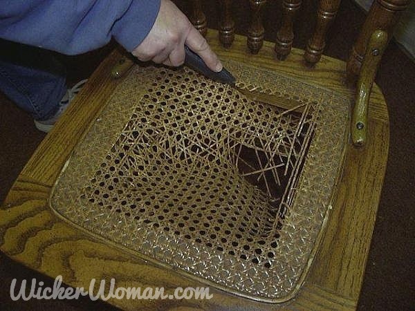 Removing old chair cane webbing with a utility knife before replacing with new spline and new caning.